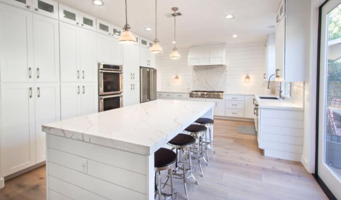 L shape kitchen design with white cabinets, large island with stacking chairs, pendent lights and spc flooring 