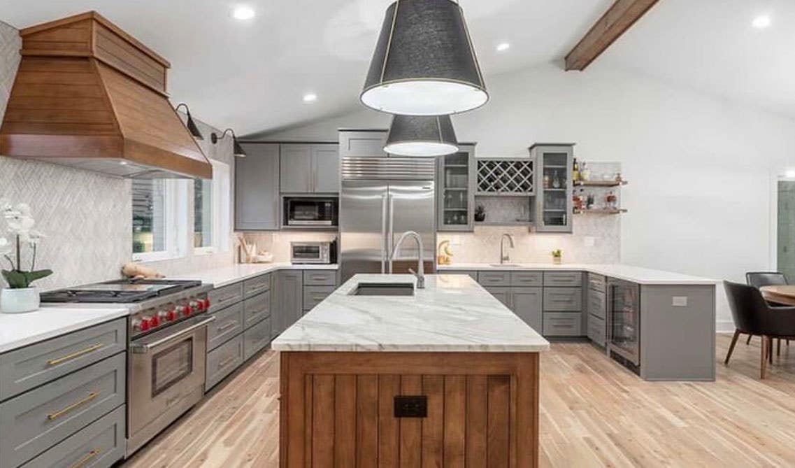 Kitchen with gray cabinets with countertop, natural wood rangehood and pattern backsplash, wooden flooring