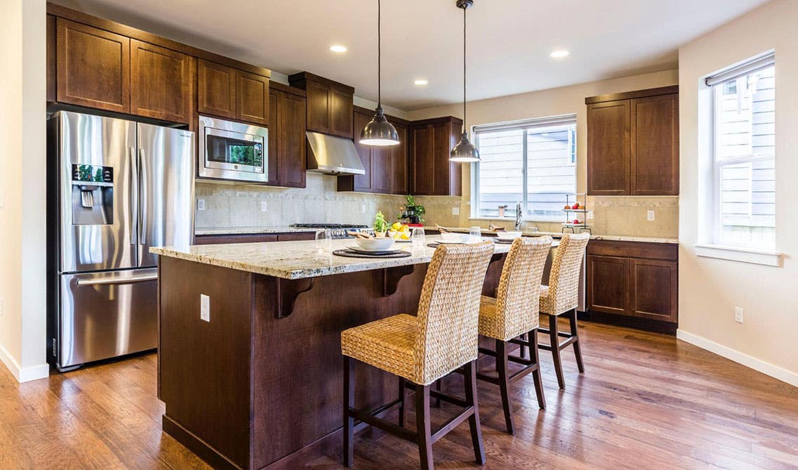 Kitchen with oak cabinets, Pendant lights above island with chairs, Marble countertop, Wooden Flooring, stainless steel appliances