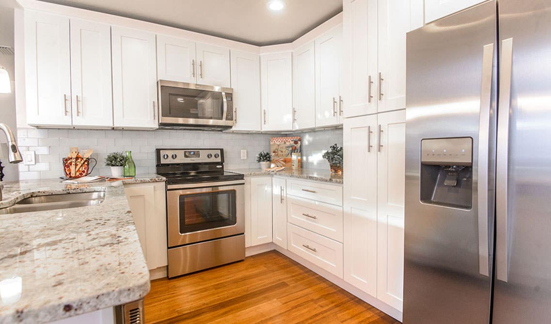 white shaker cabinets kitchen with stainless steel appliances, wooden flooring, marble countertop 