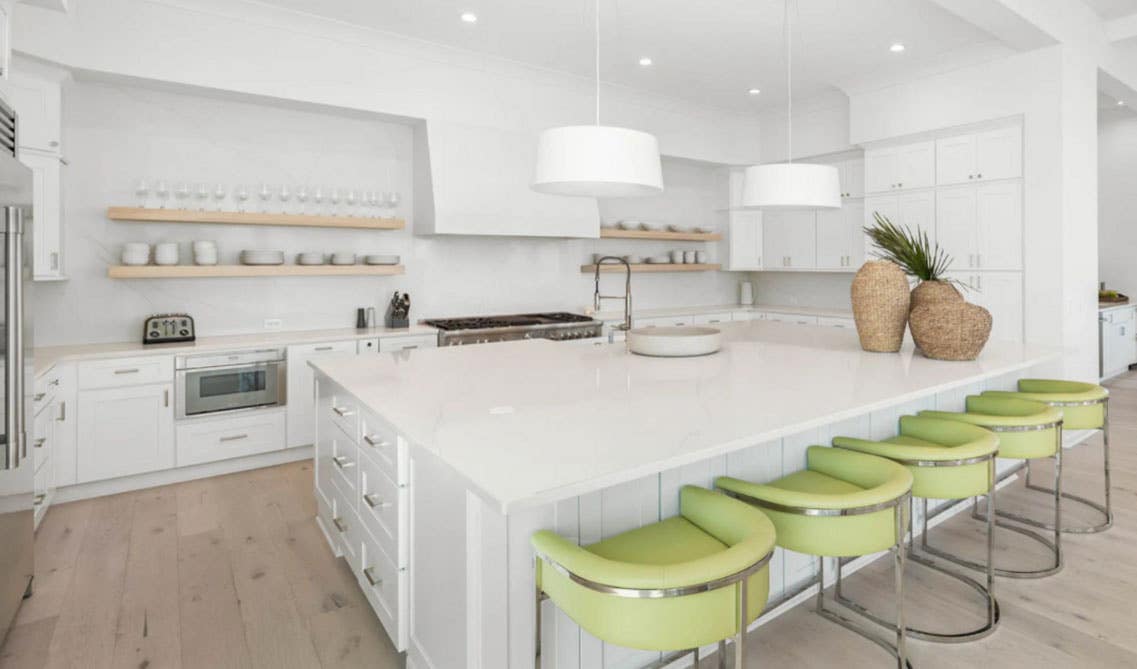 Open Style White Kitchen with Functional Large Island, Green Chairs around, Natural Wood Open Shelving's and Stainless Steel Appliances 