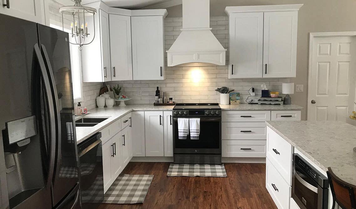 L-shaped kitchen features white cabinets, wood range hood, and large island