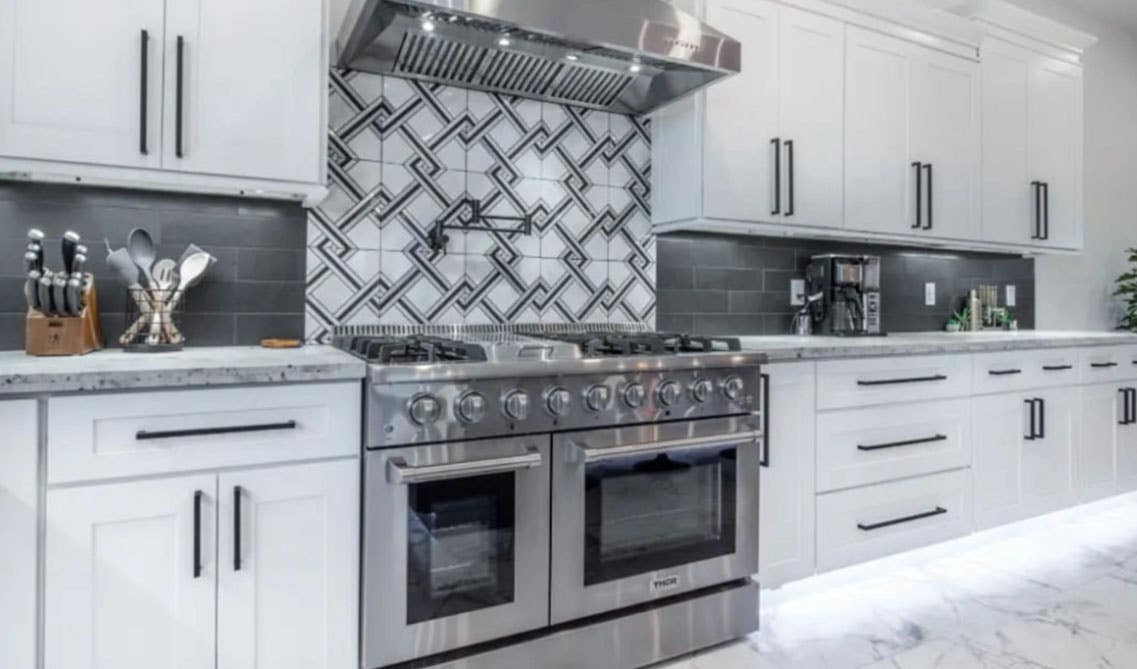 white cabinet kitchen with black hardware, stainless steel appliances, grey subway tile and pattern tile backsplash and under cabinets LED Lights