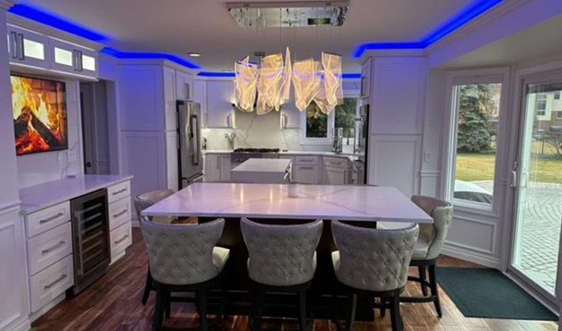 modern white kitchen with shaker cabinets, LED lights above crown molding, small island with marble counter top and wooden flooring