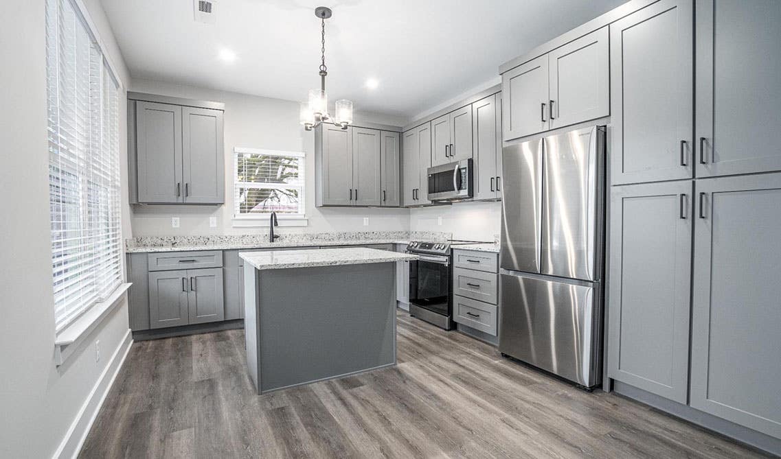 L shape kitchen design with gray shaker cabinets, small island, stainless steel appliances and scp flooring