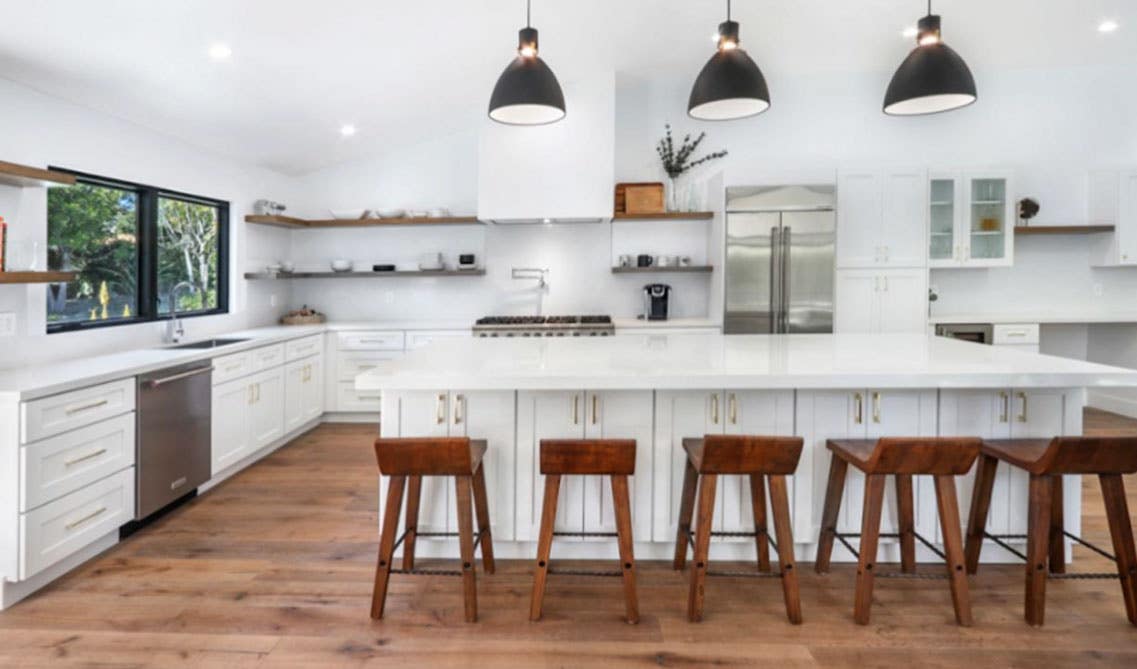 Beautiful white kitchen with shaker cabinets, large island with wood stools, floating shelves and matt black pendant lightings