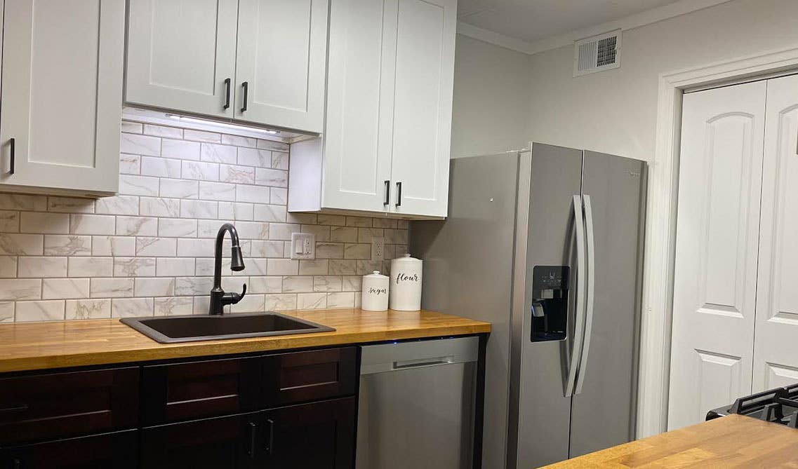 Black and white cabinets with marble backsplash and wooden countertop