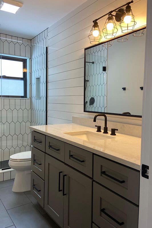 Modern bathroom design with grey vanity with matte black pulls, white marble countertop, separate shower space 