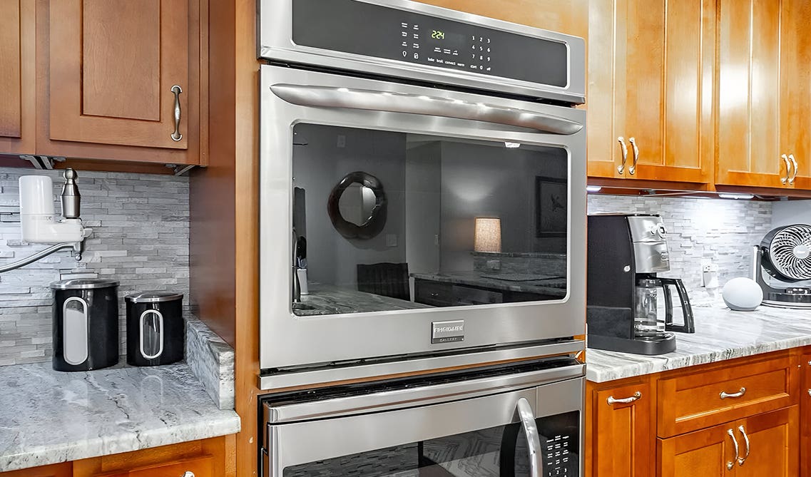Microwave brown kitchen cabinet paired with gray countertop and backsplashes 