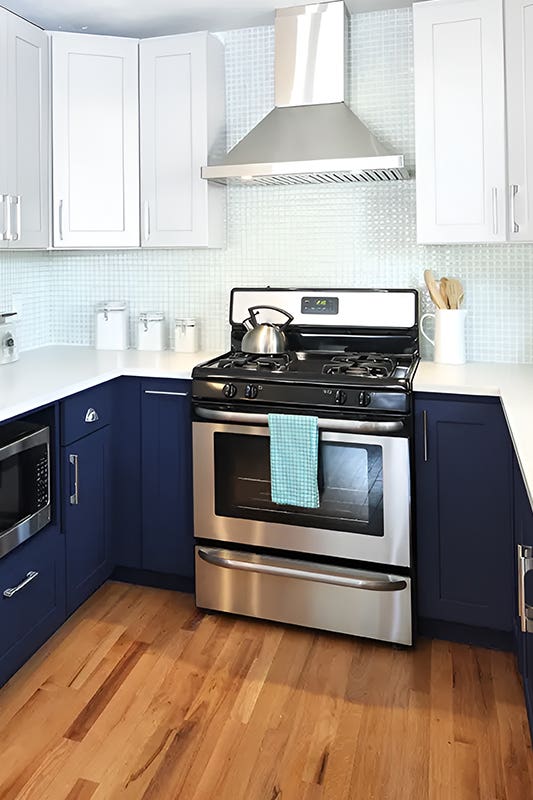 Twon tone kitchen paired with white and navy blue cabinets, white countertop, and stainless steel appliances and 