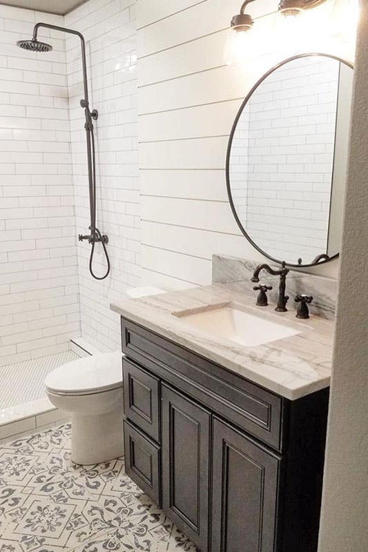 Small bathroom with black vanity with integrated sink, Round mirror on shiplap wall, Separate shower area with white subway tiles and black fixture and fitting