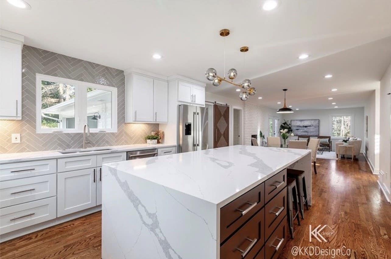 White cabinets paired with brown cabinet island, marble waterfall countertop and wooden flooring