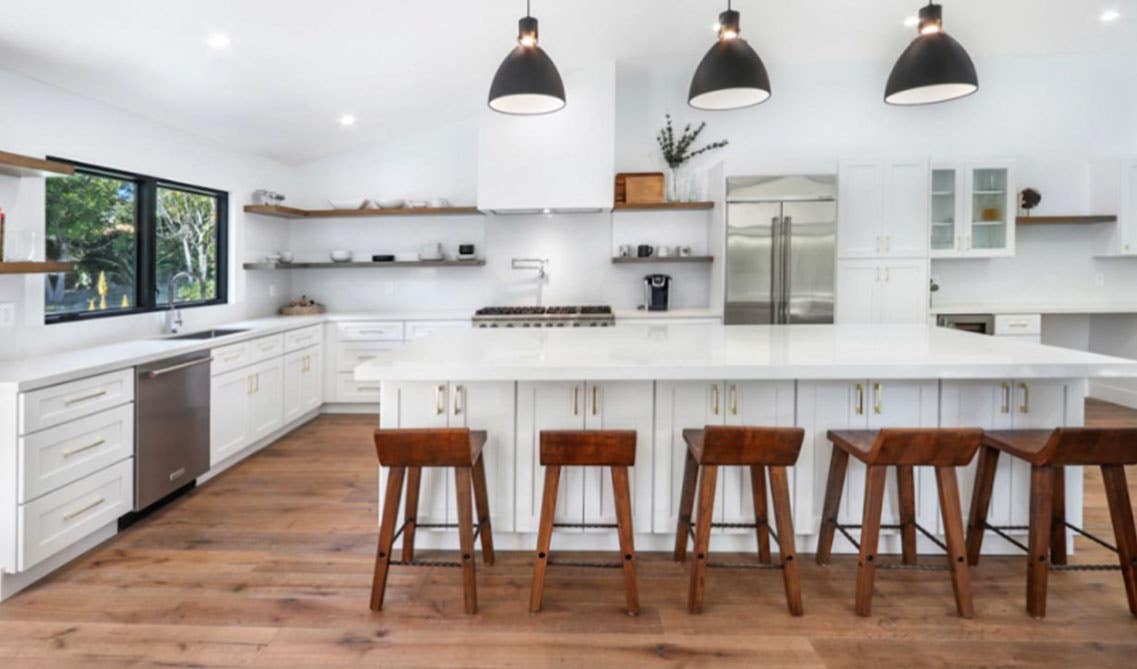 white kitchen design with different materials such as wooden shelves and chairs, brass cabinet handles, stainless steel appliances