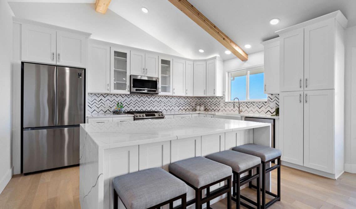 Modern Kitchen design with white cabinets and stainless steel appliances, large island with marble waterfall countertop 