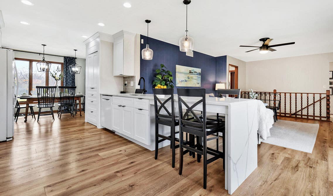 Modern Minimalist kitchen design features white cabinets with white waterfall quartz countertops, navy blue accent walls, and stainless steel appliances