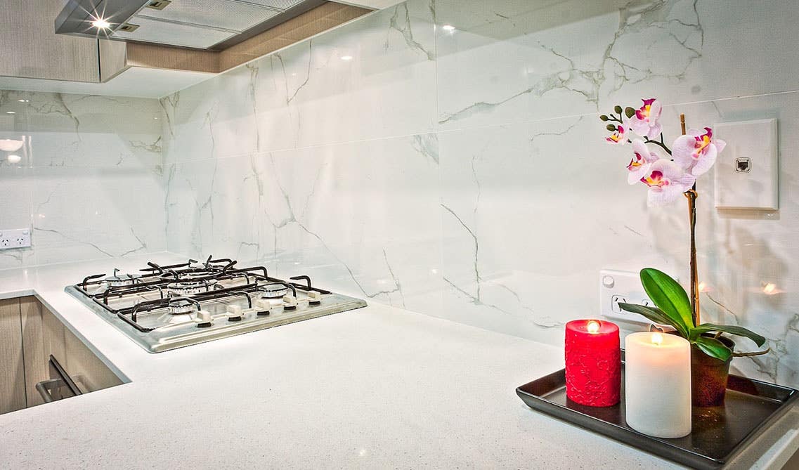 marble backsplash, stainless steel stove, white countertop and scented candle tray 