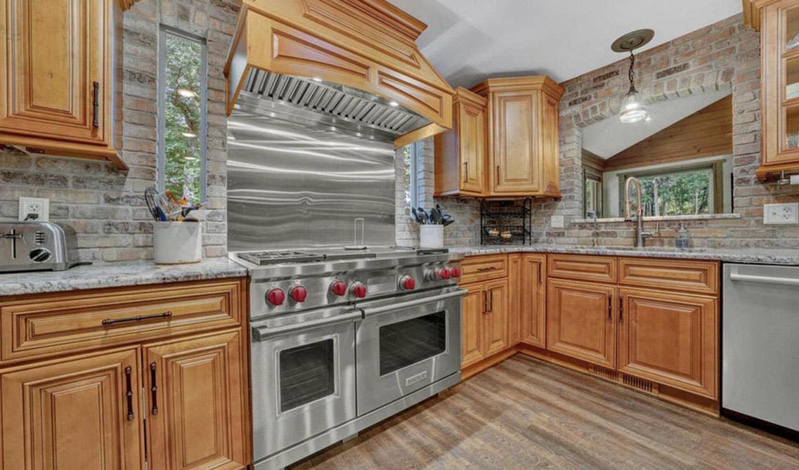 Natural wood cabinets with marble countertop, stainless steel appliances, and wooden flooring 