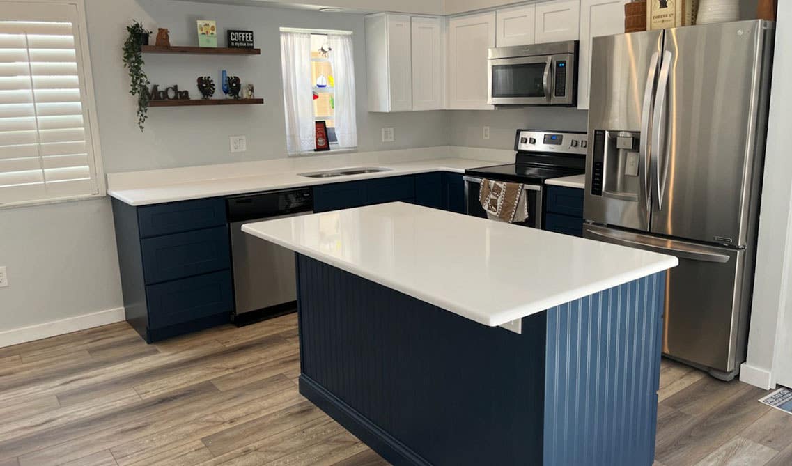 Beautiful kitchen with white and navy blue cabinets, marble countertop, wooden flooring and stainless steel appliances