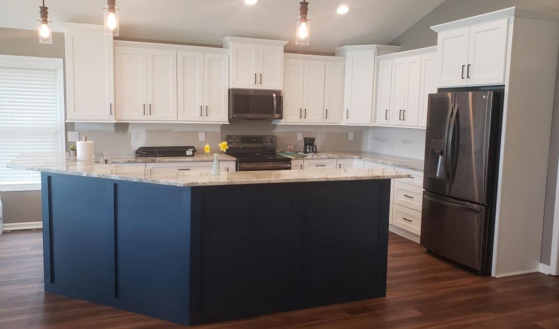 A bin kitchen with white and navy blue two toned kitchen cabinets with, wood cabinets, marble countertops and stainless steel appliances 