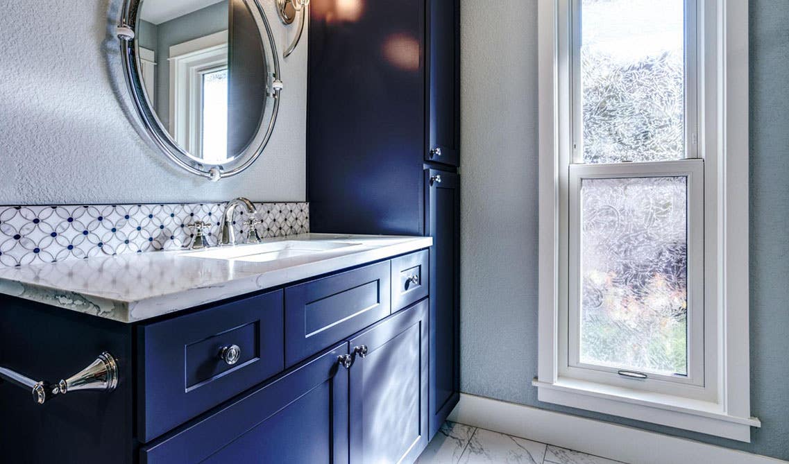 Navy blue shaker vanity cabinets with glass knobs, white countertop, round mirror and wall lamp