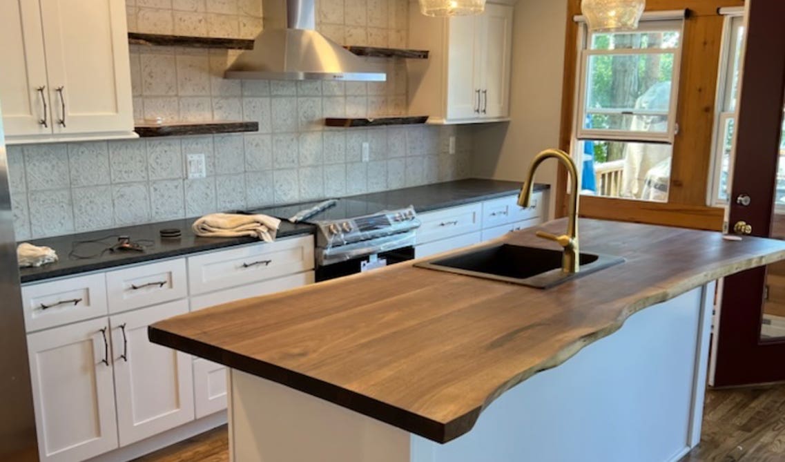 One wall kitchen design paired with white cabinets, black countertops, small island with integrated sink and open shelving