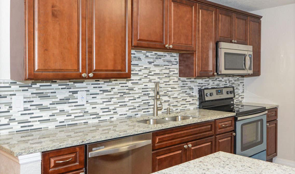 One wall kitchen with brown cabinets, marble countertop with undermount stainless steel sink, tile backsplash