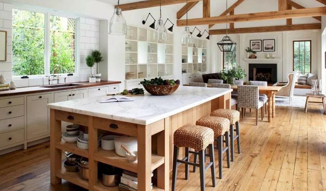 Open rustic kitchen with white cabinets and wood island, marble countertop, wooden slabs on ceiling, wooden flooring