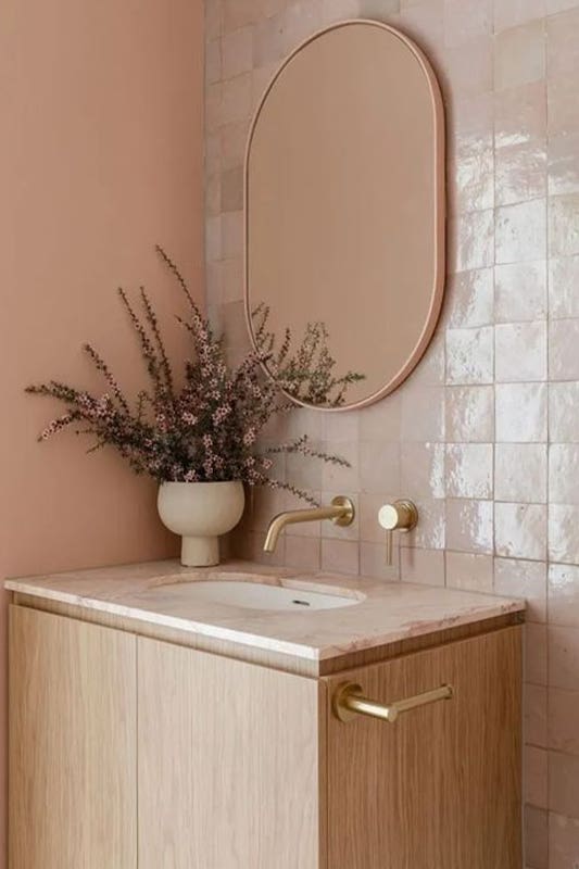 Pale peach bathroom paired with light wood vanity and gold accent 