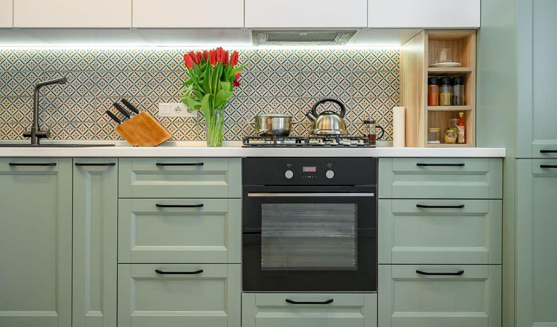 Pistachio Green kitchen Cabinets with black hardware, quartz countertops and pattern tile backsplash 