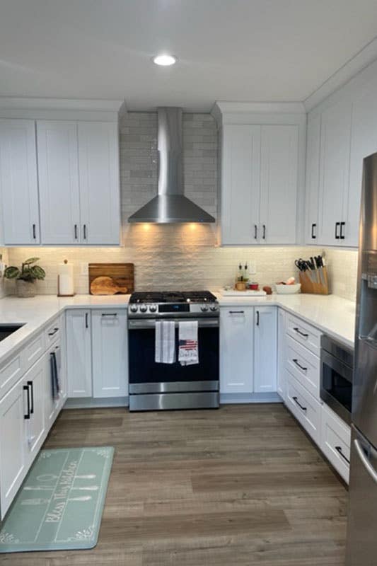 river rocks backsplash paired with white cabinets, stainless steel appliances and marble countertop 