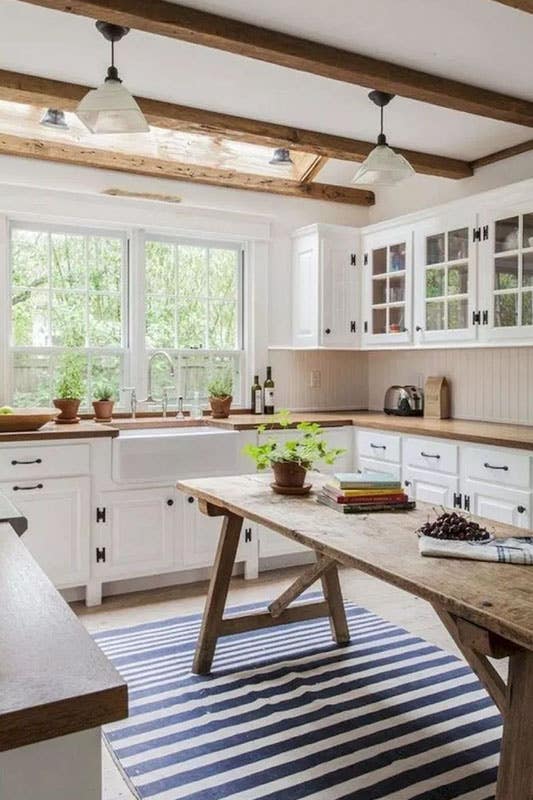 Rustic farmhouse kitchen with striped rug, white cabinets, black hardware, vintage wood table and porcelain farmhouse sink