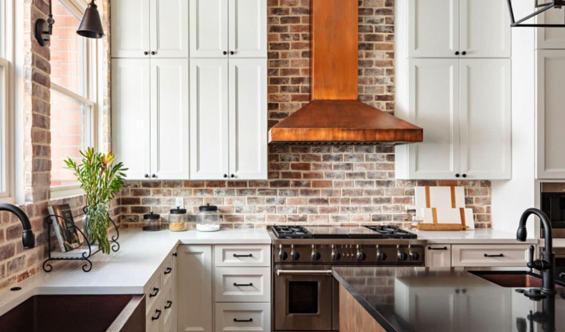 Rustic kitchen design with white cabinets, metal range hood, and brick style backsplash 