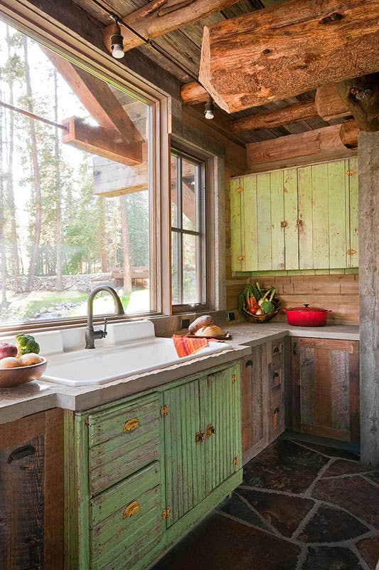Old rustic cabin country farmhouse kitchen with mismatched green and dark wood cabinets, stone floor and farmhouse sink