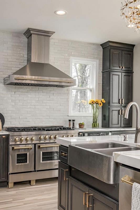 Rustic kitchen style with black cabinets, gold decorative hardware, island with farmhouse sink, ;tile backsplash and wooden flooring