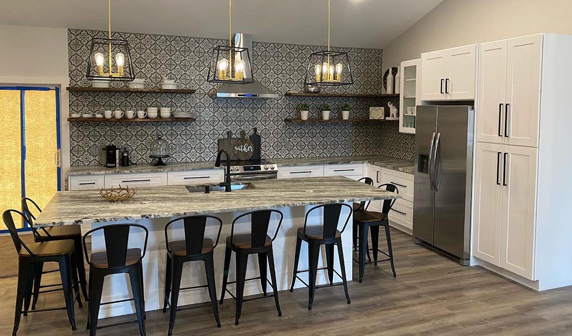 white cabinets kitchen with black accents, pendent lights, large island with sink and metal chair