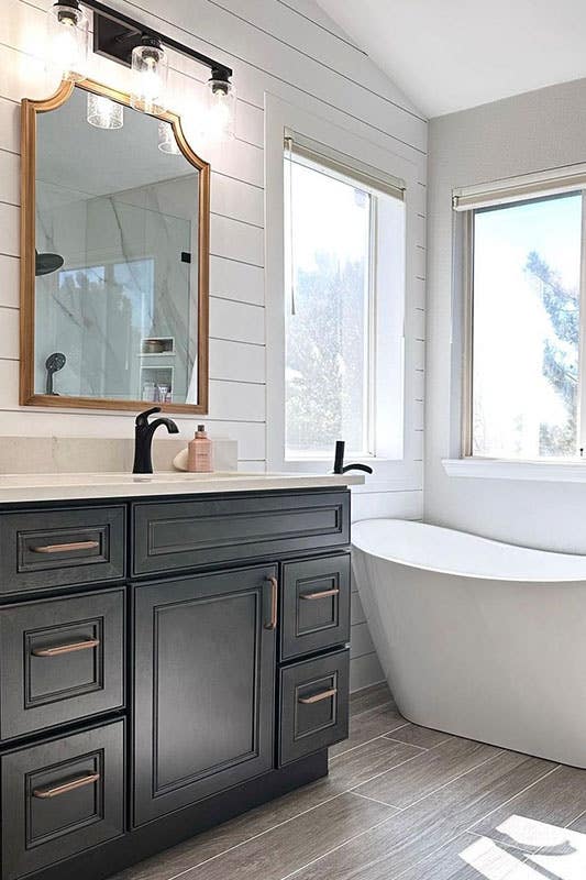 contemporary Bathroom design features Black vanity with white countertop and freestanding bathtub beside window