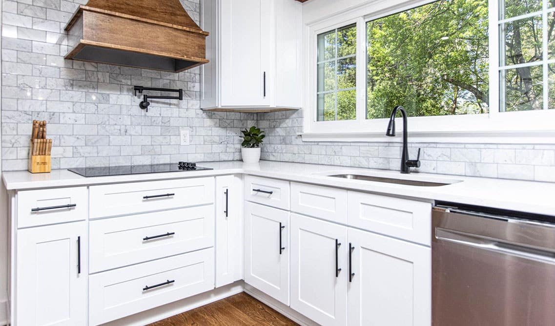 Farmhouse Kitchen with white cabinets and black hardware, wood hood, and large window