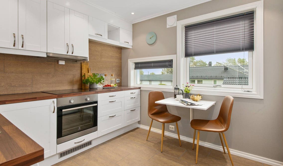 Small kitchen with white cabinets and wooden countertop and 2 chair table 