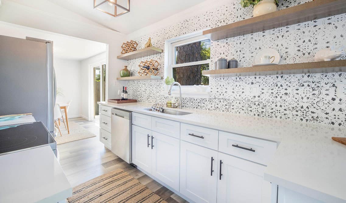 Small white kitchen with shaker cabinets, white marble countertop and wooden floating shelves, window above sink