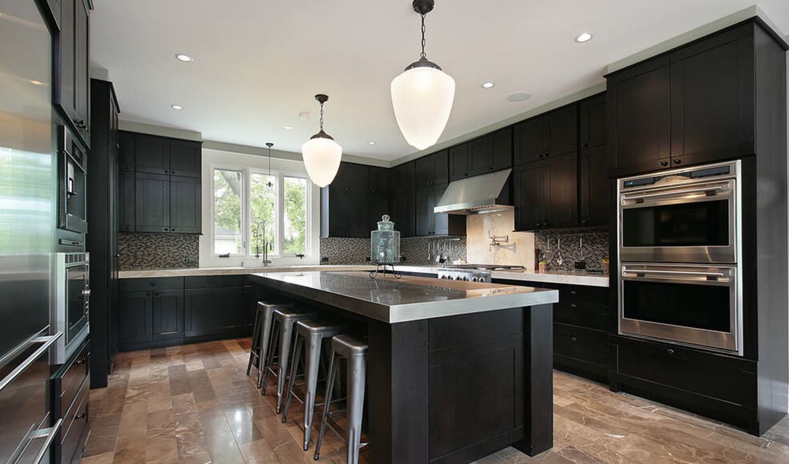 black kitchen boasts all stainless steel finishes, with metal barstools and grey countertops