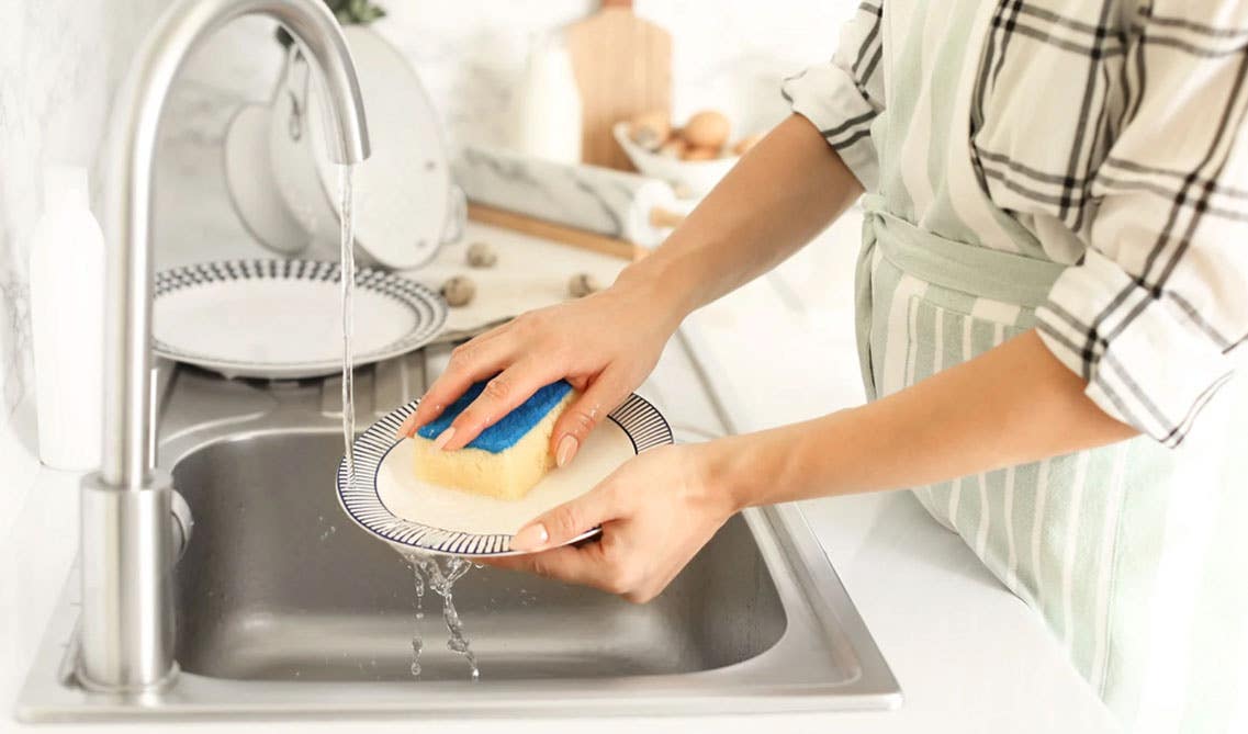 A lady washing dishes in stainless steel sink