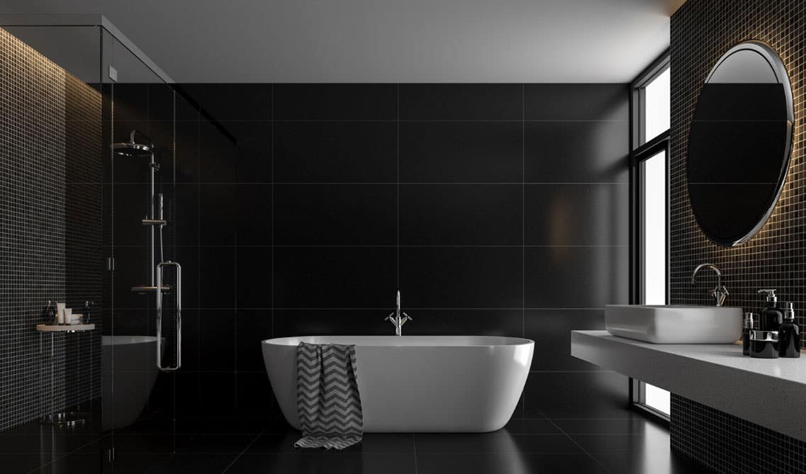 Dark theme bathroom features freestanding white bathtub, single sink with round mirror and black tile on floor and wall