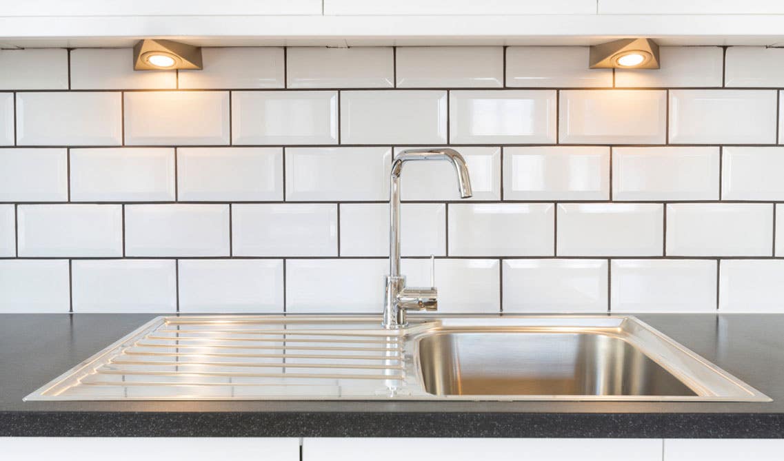 Stainless steel sink with black countertop and white subway tiles