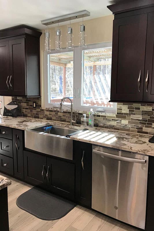 kitchen design with brown cabinets with marble countertop, stainless steel appliances, Farmhouse sink, and mismatched backsplashes 