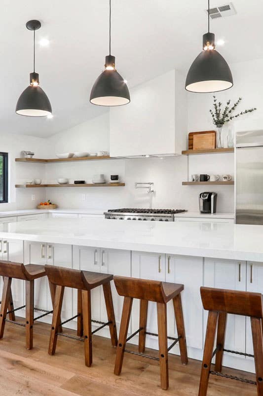 white kitchen cabinets with large island, white countertop, wood chairs, open shelvings and pendant lights