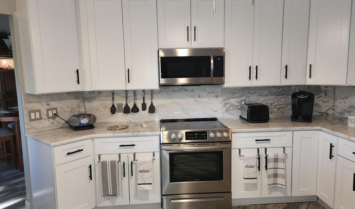 White kitchen cabinets with stone slab backsplashes and stainless steel appliances 