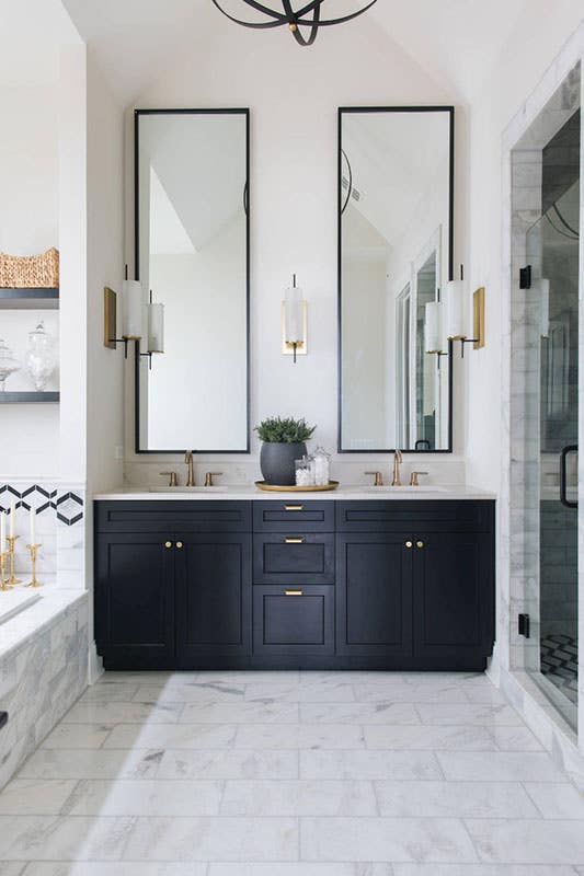 bathroom with black cabinets, large rectangular mirrors, white marble floors and brass hardware