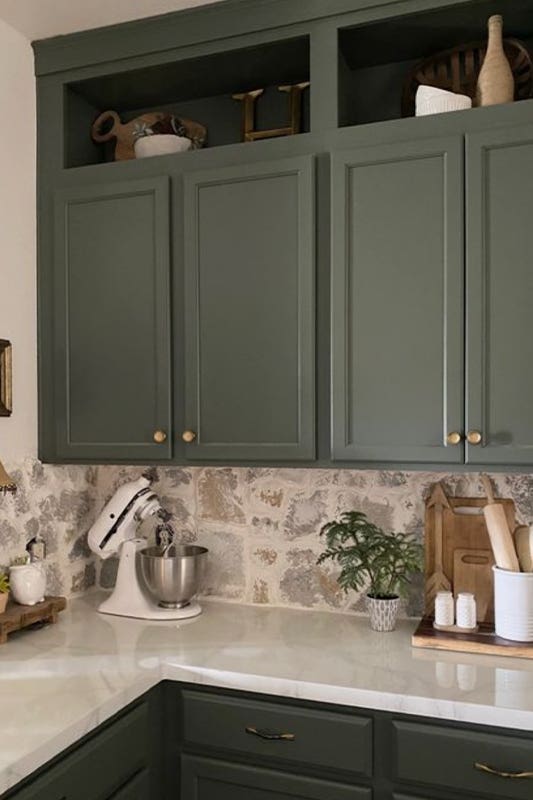 Green kitchen cabinets paired with white countertop and printed backsplash