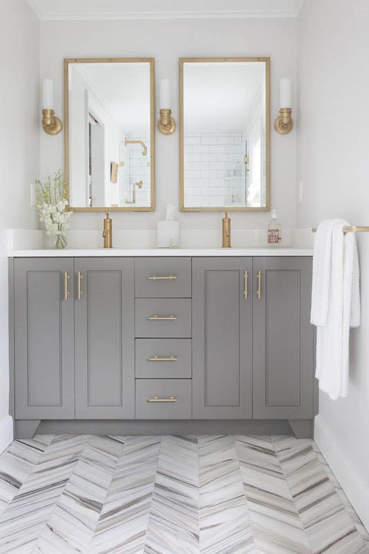 grey bathroom vanity with white countertop, brass hardware and herringbone tile flooring