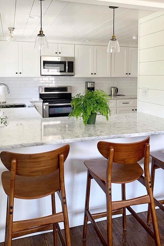 White kitchen with shaker cabinets and marble countertops, wood chair and potted plant